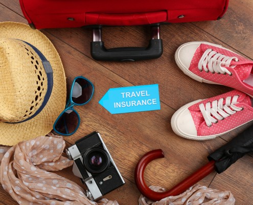 Suitcase and tourist stuff with inscription travel insurance on wooden background