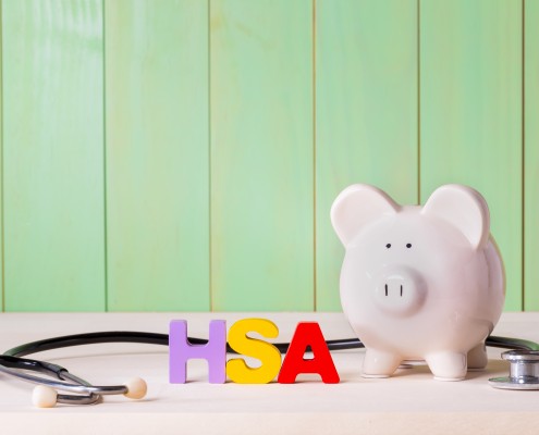 Health Savingins Account HSA concept with white piggy bank, stethoscope wood block letters and green background